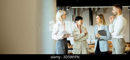 Four business professionals are having a discussion in a stylish office. They are exchanging ideas and sharing insights, with a focus on collaboration Stock Photo