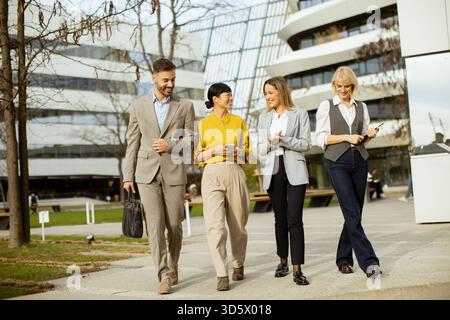 Four professionals in business attire stroll together in an urban area. They appear engaged and happy, showcasing teamwork and collaboration. The mode Stock Photo