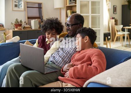 Senior Black Man Sitting with Two Children Using Laptop and Smiling Together Stock Photo