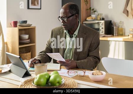 Mature Black Man Reviewing Financial Documents While Using Digital Tablet Stock Photo