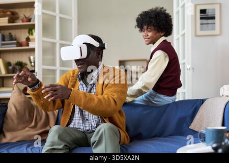 Mature Black Man Experiencing Virtual Reality While Teenager Watching Stock Photo