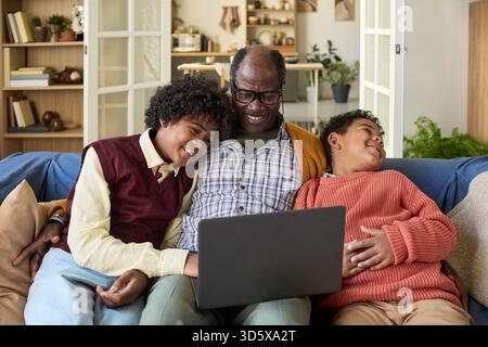 Mature Black Man Sitting with Two Children Using Laptop Smiling Together Stock Photo