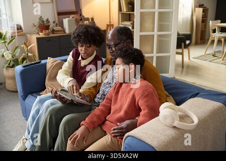 Mature Black Man Sitting with Two Children Using Digital Tablet Together Stock Photo