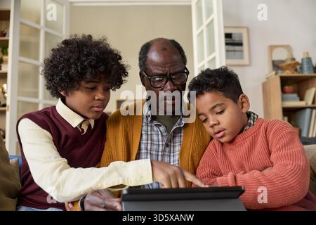 Senior Black Man Teaching Two Black Boys Using Digital Tablet at Home Stock Photo