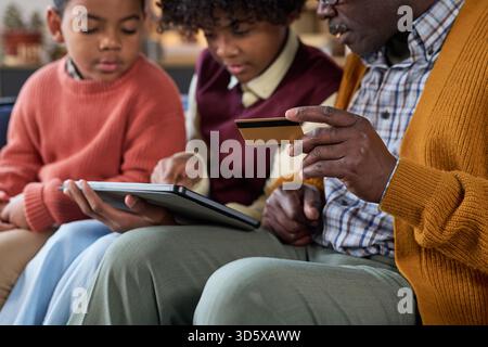 Mature Black Man Teaching Children Online Shopping Using Tablet Device Stock Photo