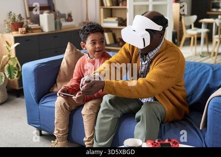 Mature Black Man Using Virtual Reality Headset Sitting with Boy Stock Photo