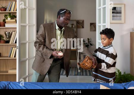Mature Black Man Teaching Boy Catching Baseball Indoors Stock Photo