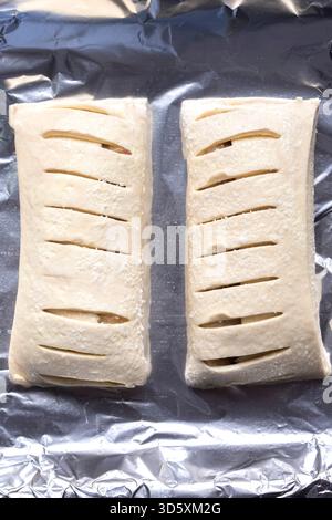 Raw apple strudels, with sliced pastry, on foil ready for cooking in an oven. Home baking concept Stock Photo