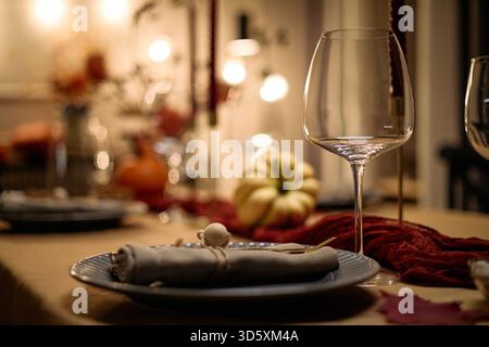 Closeup of elegant table setting with empty wine glass, ceramic plate, cloth napkin and decorative pumpkin on festive dining table prepared for Thanksgiving dinner among friends Stock Photo