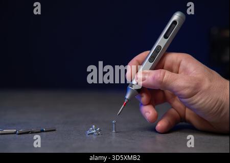 precision electric screwdriver and bits displayed on textured dark surface, product showcase for tool designer, cool blue rim lighting, scattered prec Stock Photo
