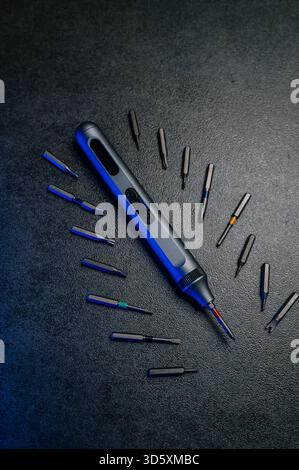 precision electric screwdriver and bits displayed on textured dark surface, product showcase for tool designer, cool blue rim lighting, scattered prec Stock Photo