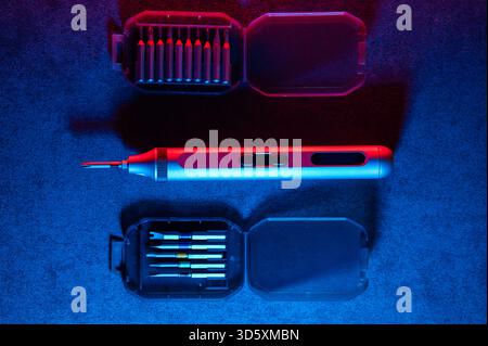 precision electric screwdriver and bits displayed on textured dark surface, product showcase for tool designer, cool blue rim lighting, scattered prec Stock Photo