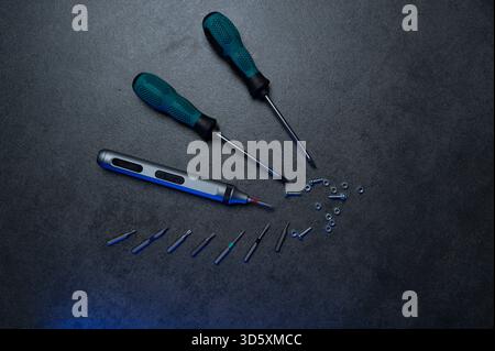 precision electric screwdriver and bits displayed on textured dark surface, product showcase for tool designer, cool blue rim lighting, scattered prec Stock Photo