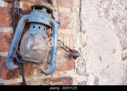 Rusty old damaged kerosene lamp on a wall, selective focus. Stock Photo