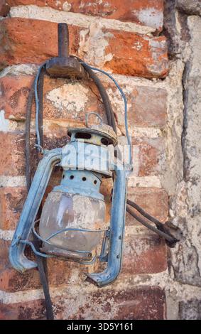 Rusty old damaged kerosene lamp on a wall, selective focus. Stock Photo
