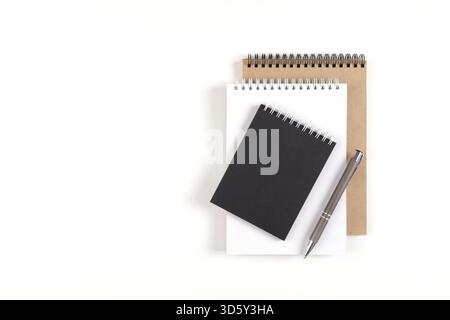 Three blank notepads on a spiral stacked in a stack on a white background. Notebooks with white, black and recycled sheets and pen. Education, office Stock Photo