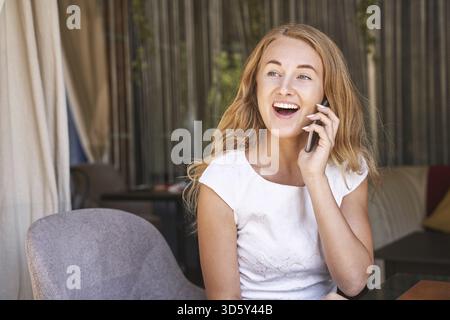 Pretty young woman talking by phone. Happy female person outdoors. Summer business portrait. Lady calling friends or boyfriend. Blonde long hair. Cute Stock Photo