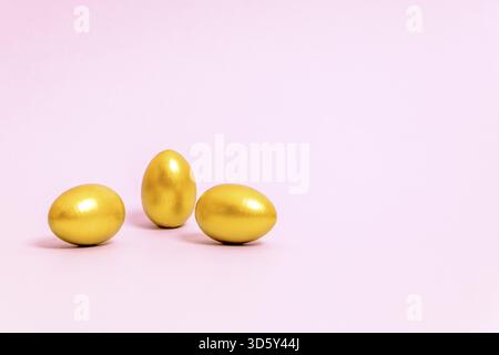 Three Easter eggs decorated with gold paint on a pink background. Concept for Easter, spring. Selective focus. Copy space Stock Photo