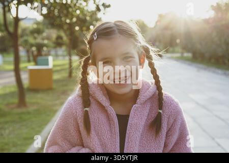 Portrait of a laughing funny cheerful girl 6 years old in the park at sunset, missing front tooth Stock Photo