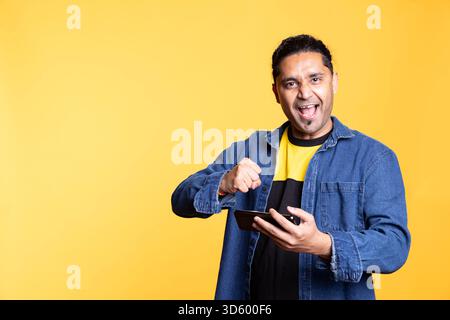 Satisfied pleased guy winning video games and feeling thrilled with the competition, enjoying interactive online multiplayer game for entertainment. Young indian man on studio background. Stock Photo