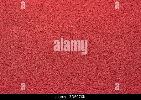 A uniformly textured background of rough granular material in a deep red color resembling the surface of stucco Stock Photo