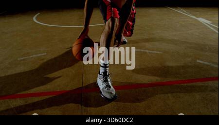 Dribbling player lower body handling ball on gym court with painted lines, wearing red shorts Stock Photo