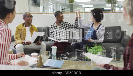 High-fiving colleagues exchanging ideas in modern office lounge, with glass table and icon overlay Stock Photo