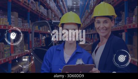 Standing two women in coveralls and blazer in yellow hard hats checking warehouse with forklift Stock Photo