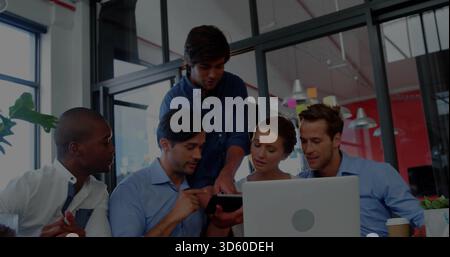 Working team in business casual leaning over laptop and tablet at open-plan office, with coffee cup Stock Photo