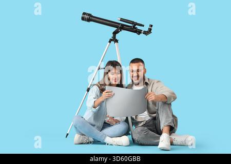 Young couple with map and telescope sitting on blue background Stock Photo