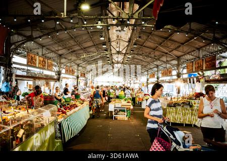 Busy indoor market in Antibes, France, with vendors selling fresh produce and shoppers walking through the historic steel-roofed market hall. Stock Photo