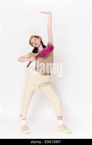 Happy, smiling young female musician with ukulele in one hand and other raised high. Positive musician poses and looks at camera, her energy radiating Stock Photo