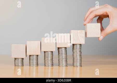 Human hand holding a wooden blocks on stack of coins on white background, Increase business capital, Invest more. Fund investment concept Stock Photo