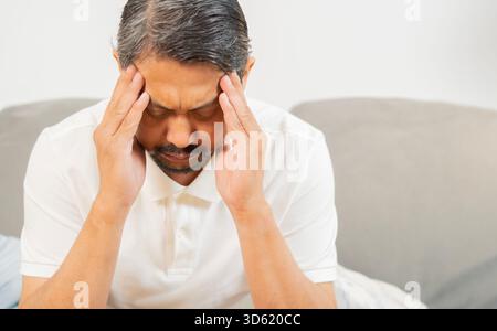 Stressed mature Asain man suffering from severe headache or migraine at home. Copy space. Health concept. Stock Photo
