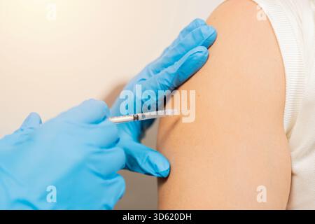 Close up of nurse hands getting vaccinated with syringe and needle. Human receiving vaccine shot from hands of doctor for virus protection. Selective Stock Photo
