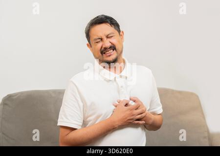 Close-up portrait photo of a stressed man who is suffering from a chest pain and touching his heart area. Heart disease concept. Stock Photo