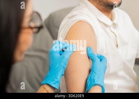 Doctor putting a bandage on the adult patient man after get a vaccinated against coronavirus at clinic. Back view, selective focus. Stock Photo