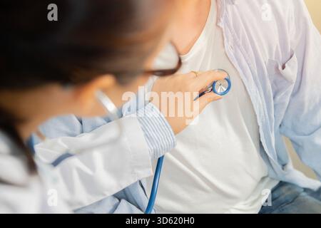 Female middle-aged doctor using stethoscope to examine patient in the hospital. Medicine concept. Selective focus. Stock Photo