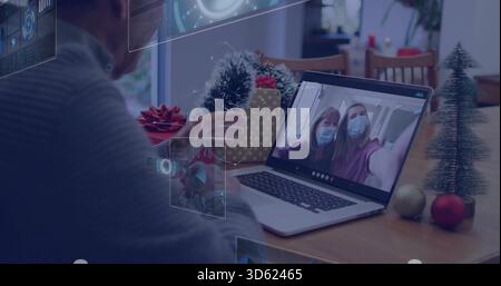 Sitting senior man in grey sweater operating laptop at dining table, showing AR UI panels Stock Photo