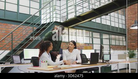 Reviewing three-person team in white blazer, green shirt, pointing at documents on laptop in loft Stock Photo