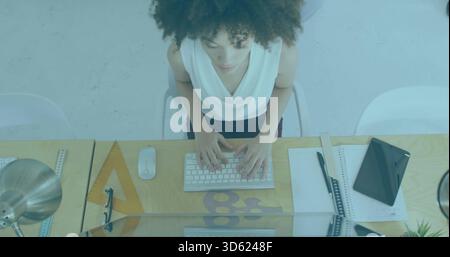 Typing woman wearing sleeveless blouse and dark skirt at wooden desk with keyboard and set square Stock Photo