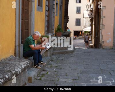 A man sitting on a door step reading the news paper in Castelnuovo Italy Stock Photo
