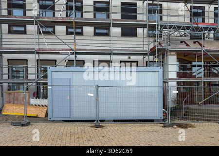 A construction site features a large storage container surrounded by scaffolding. Workers are busy on the upper levels of the building, indicating ong Stock Photo
