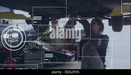 Grinding mechanic in apron and gloves using grinder under raised car in garage, producing sparks Stock Photo