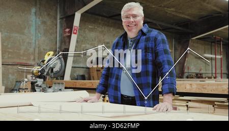 Smiling woodworker in plaid shirt and safety glasses at bench in warehouse with line-chart overlay Stock Photo