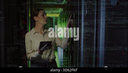 Diagnosing IT pro in biz-casual clothes holding tablet, touching rack in server aisle, code overlay Stock Photo