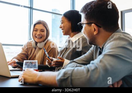 A diverse group of young adults engaged in a friendly conversation at the workplace. They appear collaborative and enthusiastic, seated together at a Stock Photo