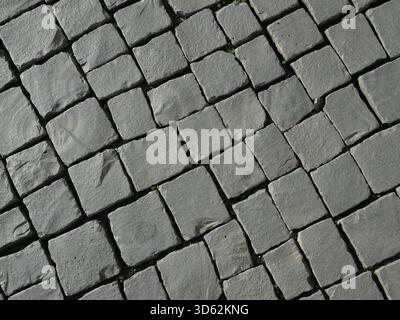 Gray natural stone mosaic pavement of basalt or granite, diagonal pattern and slight vegetation in joints. Copyspace. Stock Photo