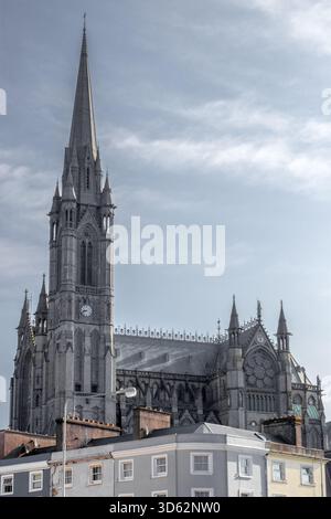 View of St. Colman's Cathedral rises majestically above colorful rooftops, its Gothic spires piercing the cloudy sky, a timeless landmark, Cobh, Count Stock Photo