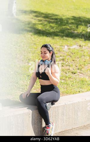 A young woman rests and relaxes with her eyes closed, sitting in the park, after exercising and playing sports Stock Photo
